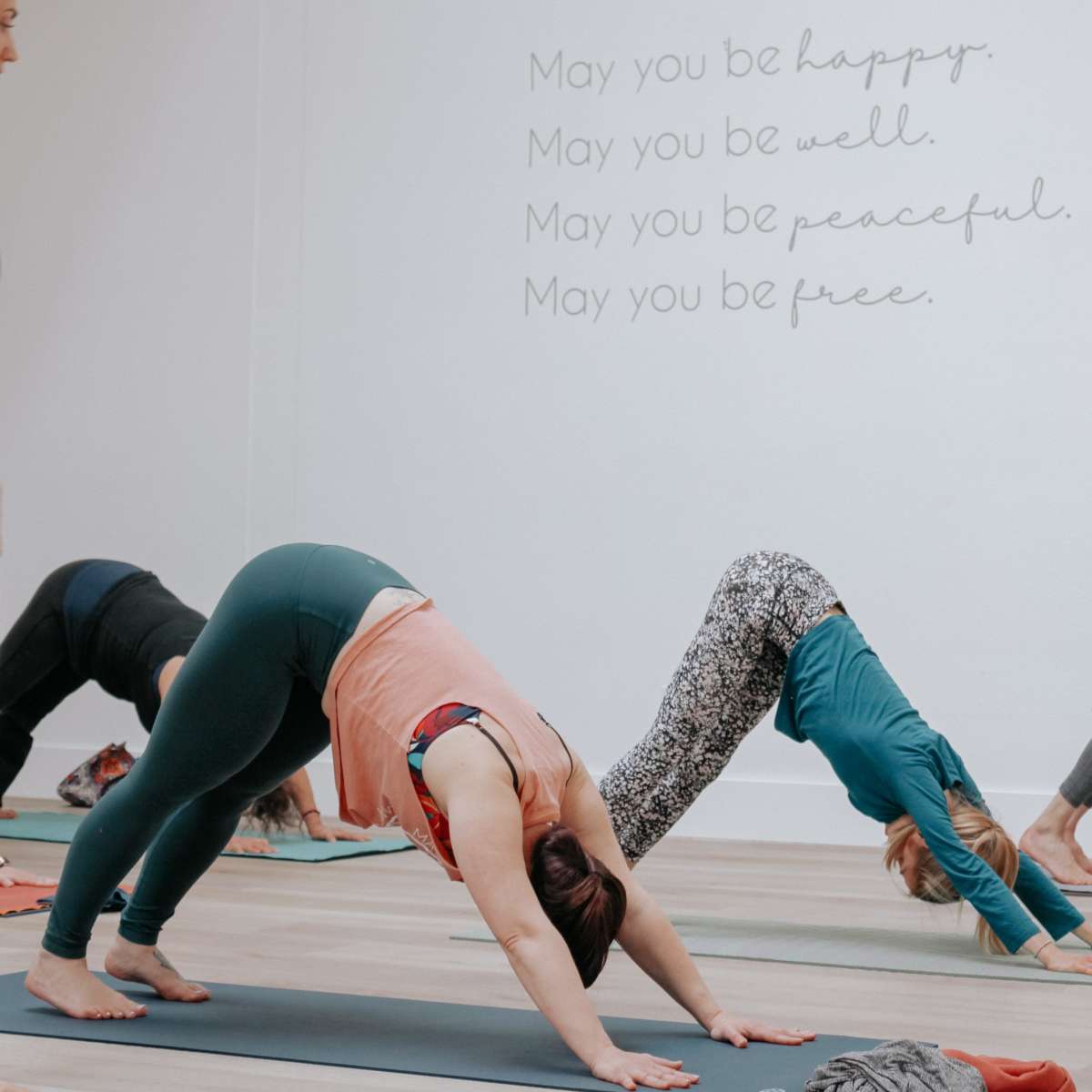 Four people are practicing yoga in a studio, performing downward-facing dog poses on exercise mats.