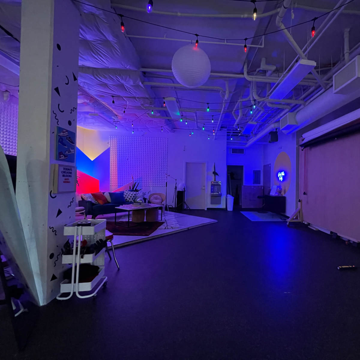 A spacious room features colorful lights, modern furniture, and various decorative elements, with a backdrop and equipment in the corner.