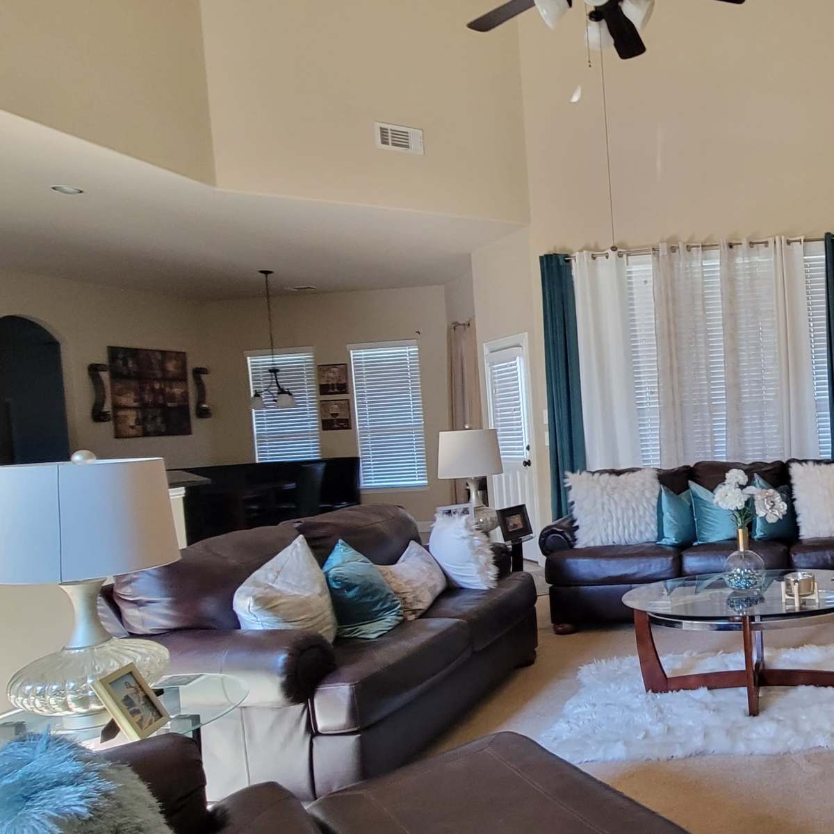The living room features two leather sofas, a glass coffee table on a rug, and large windows with blue curtains.