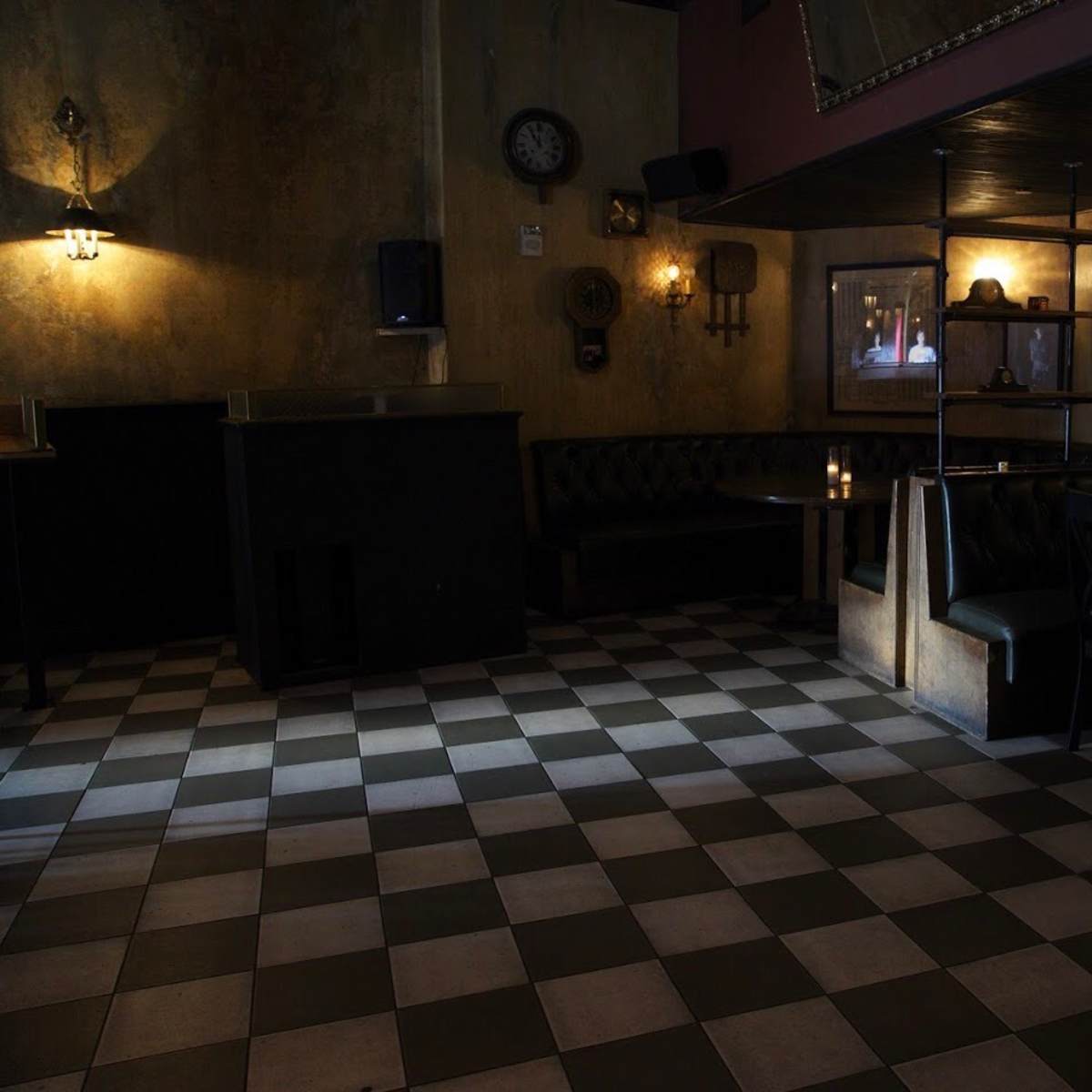 A dimly lit bar interior with checkered flooring, leather seating, and a few small tables.