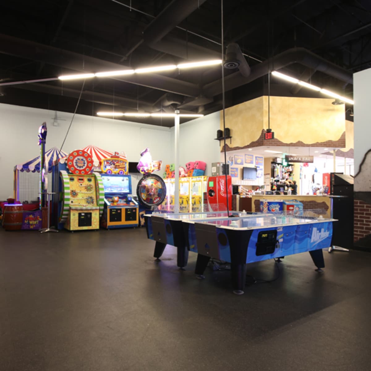 An indoor arcade featuring various gaming machines, including a blue air hockey table and colorful ticket redemption games in the background.
