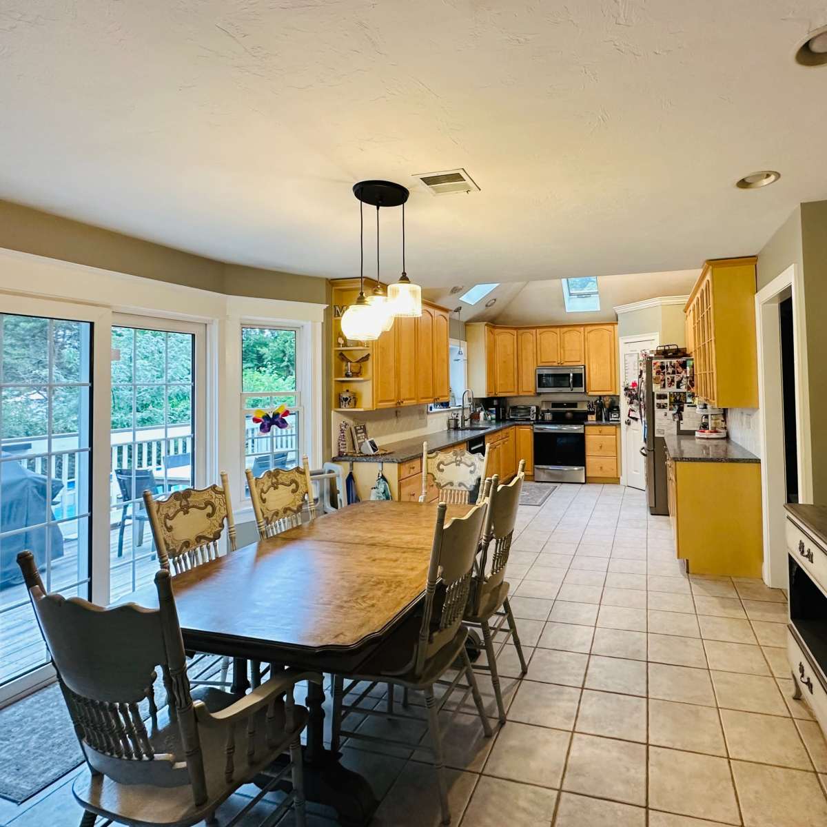 A spacious kitchen with wooden cabinets, a dining table surrounded by chairs, and large windows overlooking a deck.