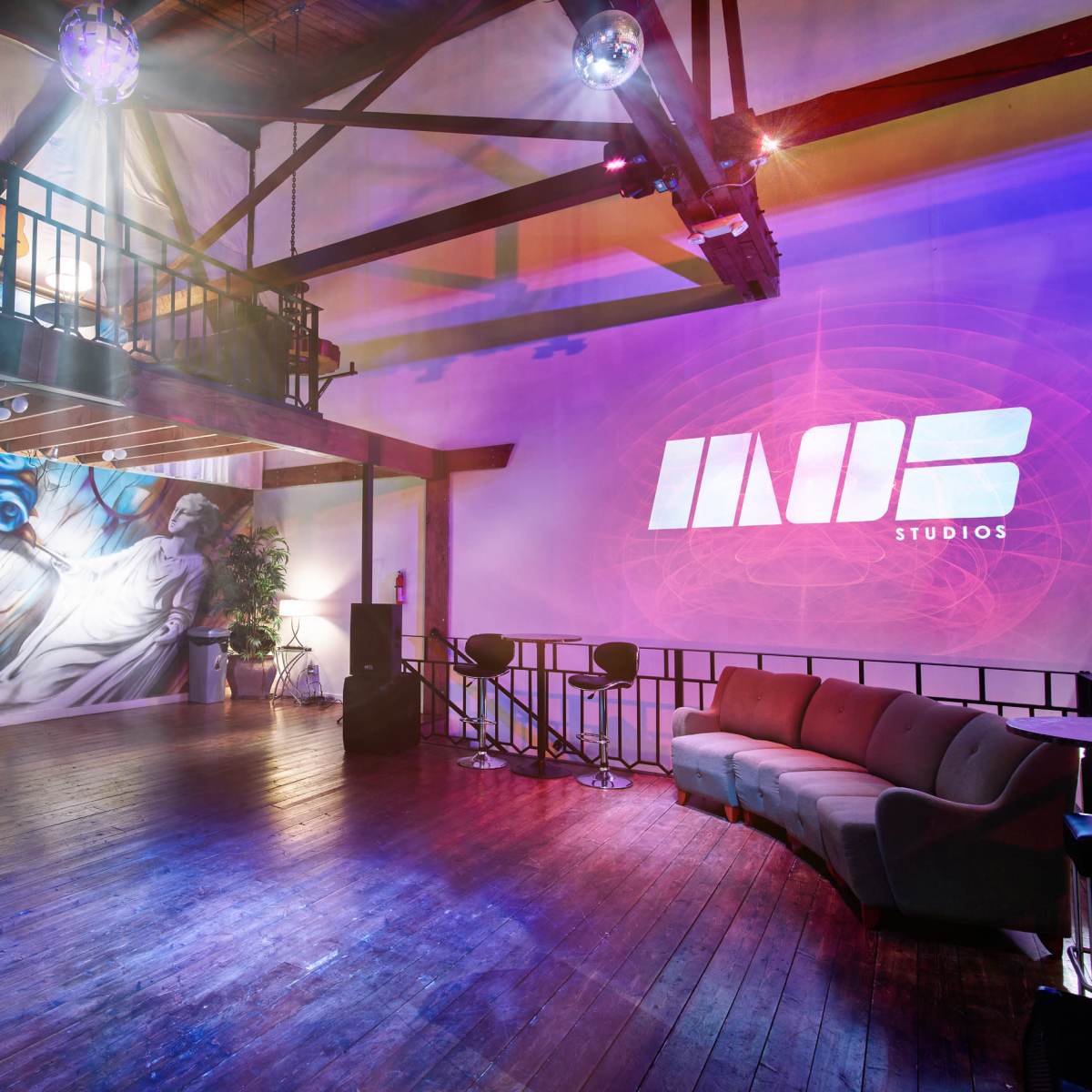 The interior of a spacious studio features a vibrant mural, modern seating, and a large projection displaying the logo "INOB STUDIOS."