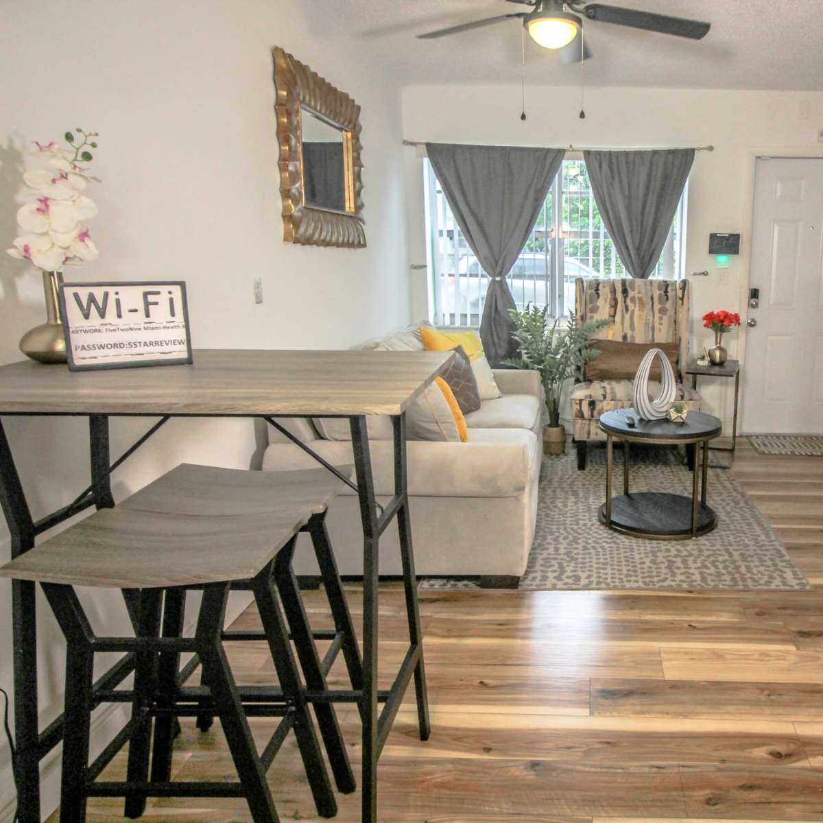 A small living room area with a gray sofa, a round coffee table, a dining set, and stairs leading to an upper level.