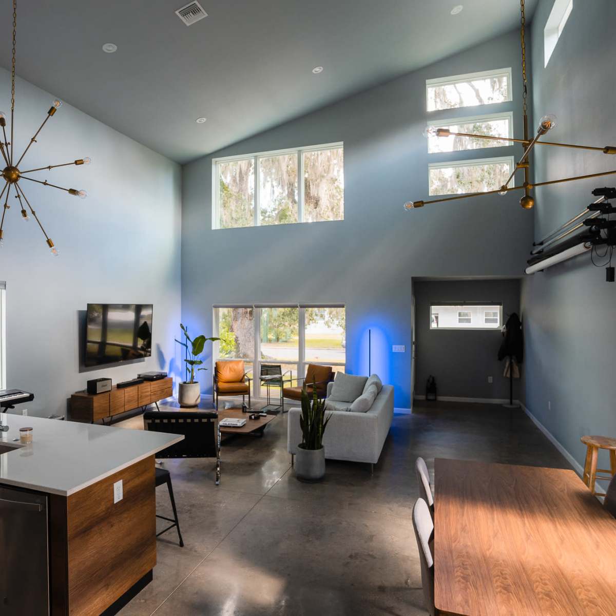A modern living space with high ceilings, a kitchen island, a dining table, and large windows allowing for natural light.