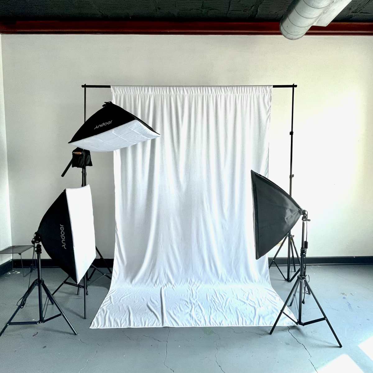 A photography studio setup with two softbox lights and a backdrop stand holding a white fabric.
