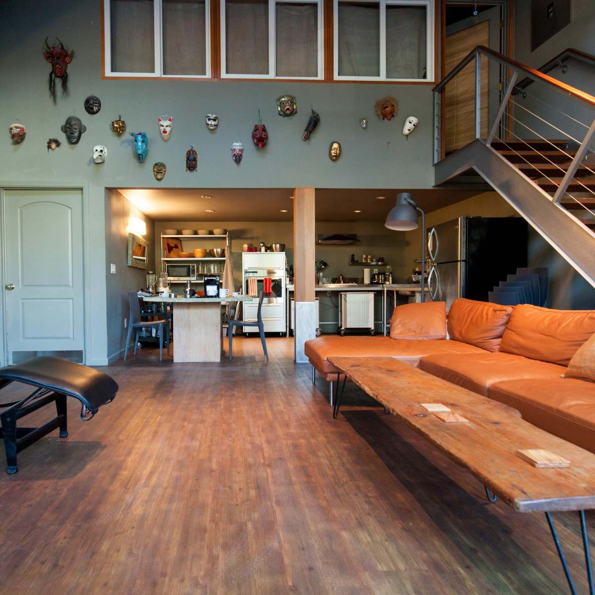 The spacious living area features a leather sectional sofa, a chaise lounge, and walls decorated with various masks, leading to an open kitchen visible in the background.