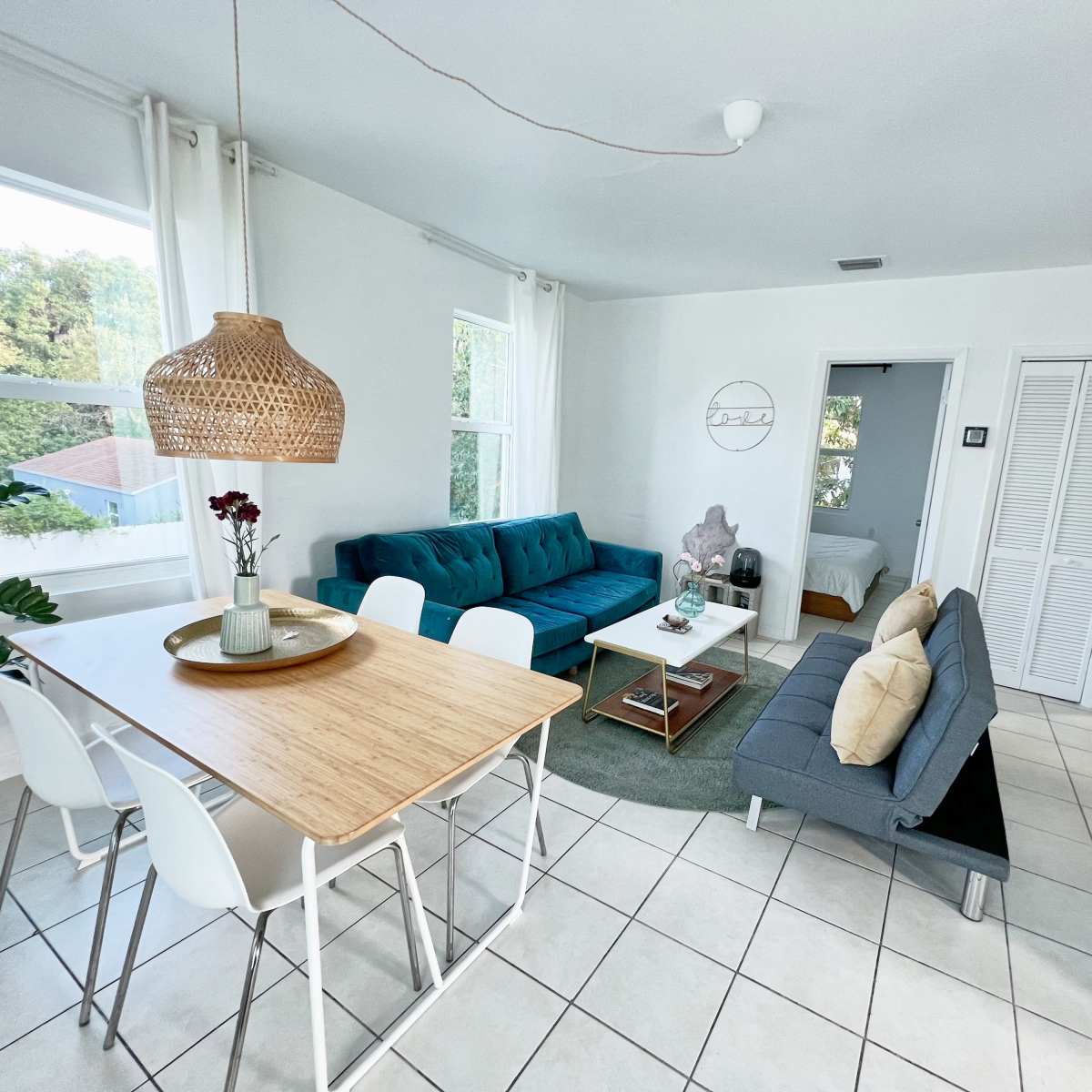 A bright, open living area featuring a dining table, two sofas in different colors, and large windows allowing natural light to enter.