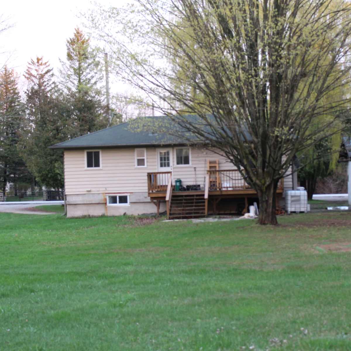 A single-story house with a front porch, surrounded by trees and a grassy yard.