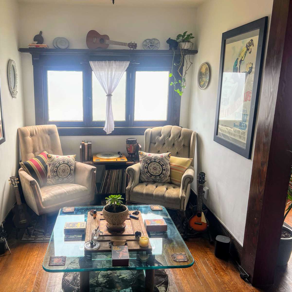A cozy corner with two armchairs facing a glass coffee table, surrounded by plants and framed artwork against the walls.