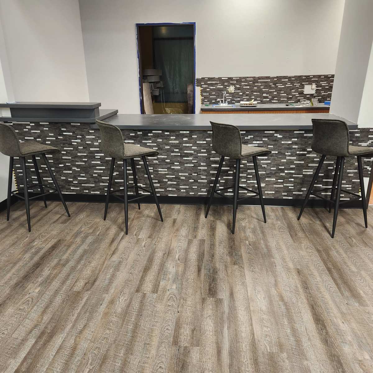A bar area with four high-backed stools arranged in front of a tiled counter against a wooden floor.