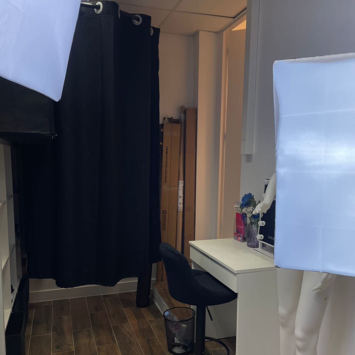 The scene shows a small room with a black curtain, a desk with a chair, and lighting equipment on either side.