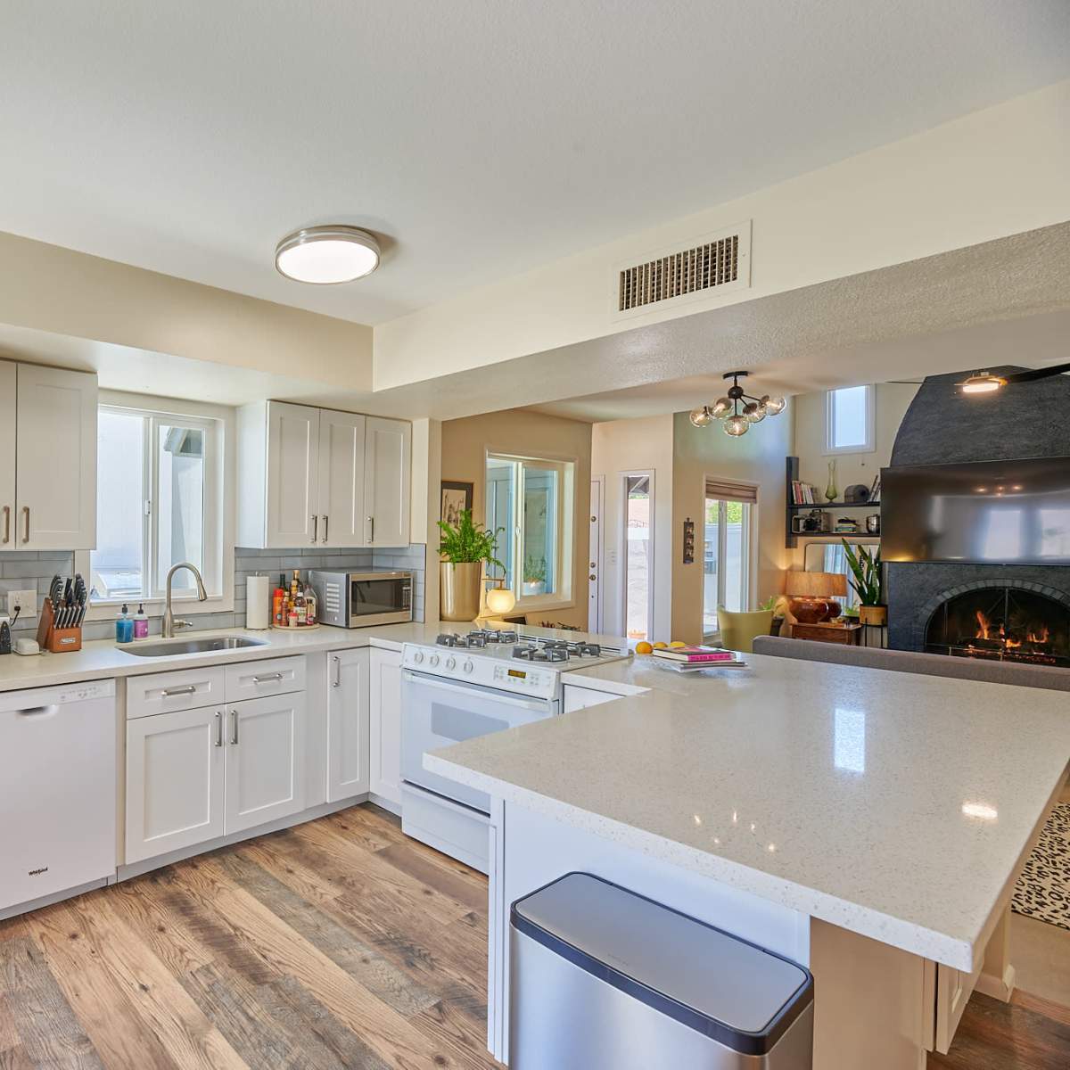 A modern kitchen with white cabinets, a countertop island, a stove, and a large window allowing natural light to enter.