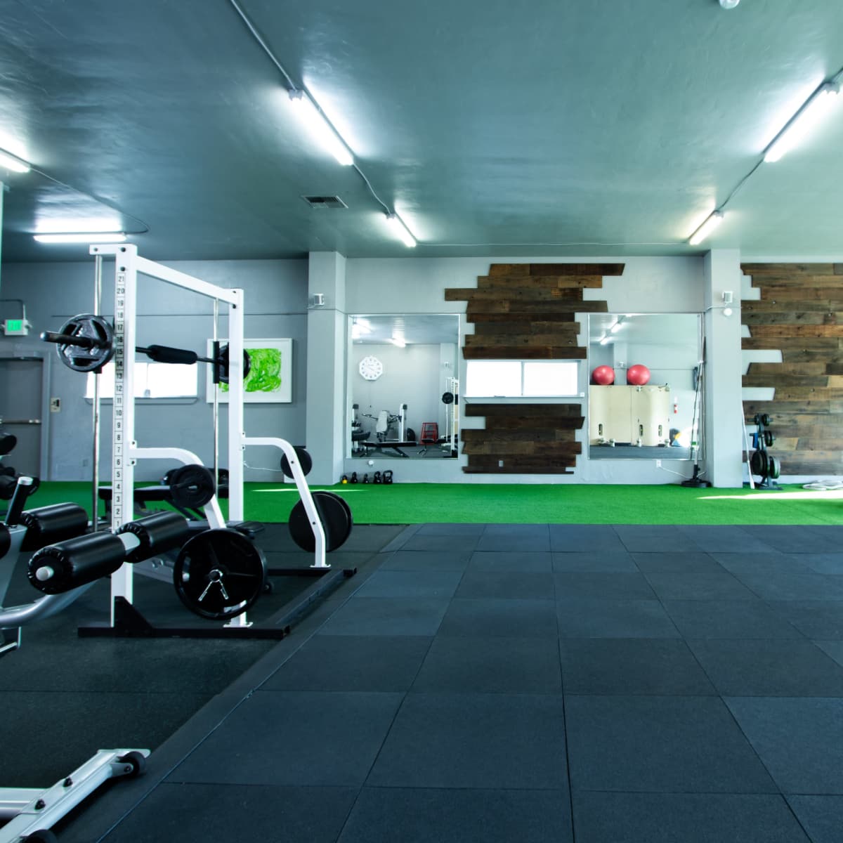 A spacious gym with weightlifting equipment, exercise machines, and a green turf area.