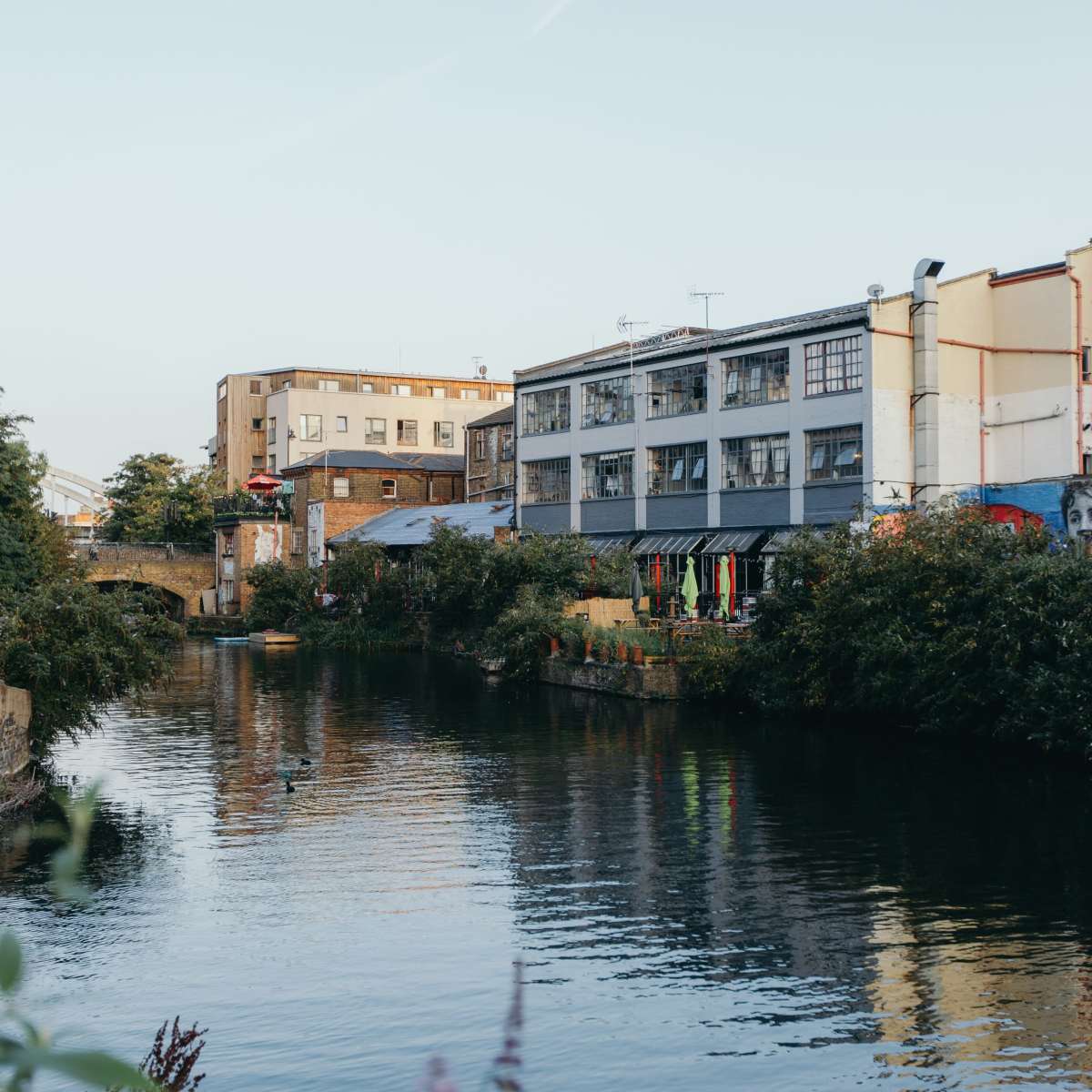 A canal lined with buildings and greenery, reflecting a clear sky above.