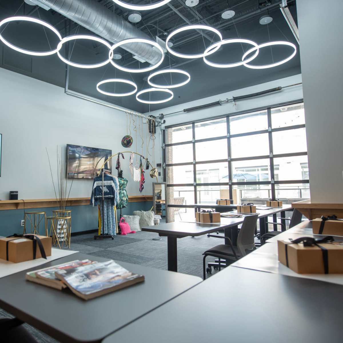 A modern interior space designed for a style therapy session, featuring a presentation screen, a TV, multiple tables set up with materials, and unique circular light fixtures on the ceiling.