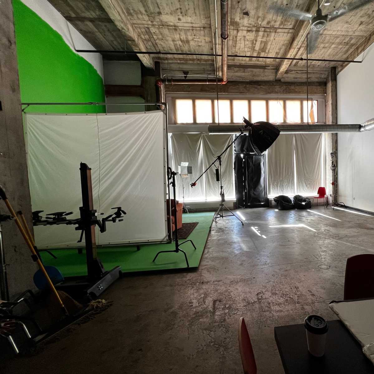 A studio space with green and white backdrops, various photography equipment, and natural light coming through large windows.