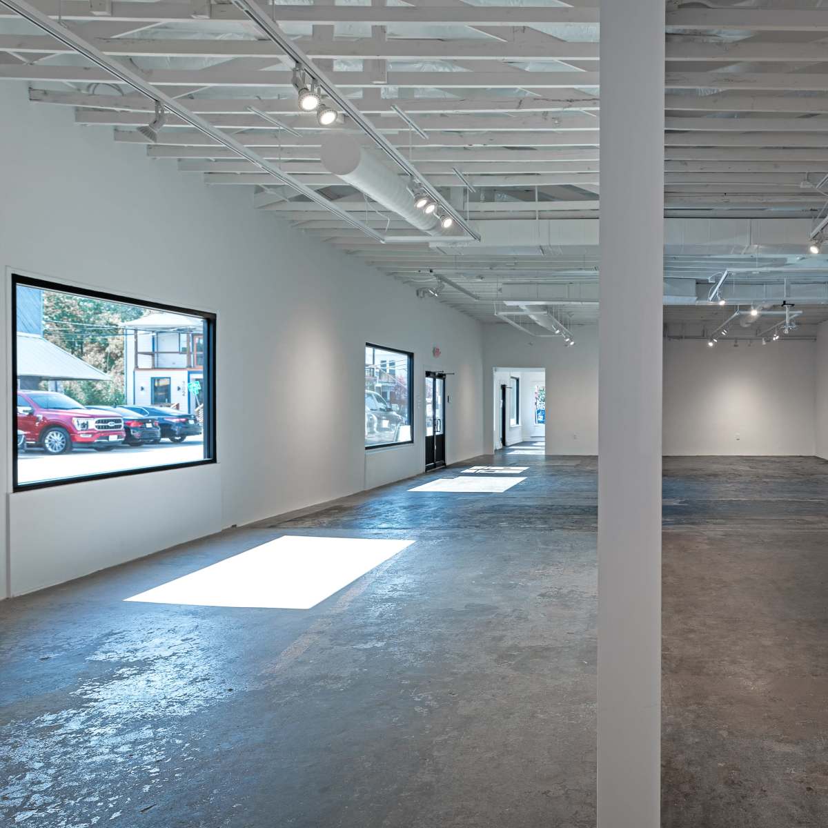 A spacious, empty gallery with polished concrete floors, bright lighting, and large windows.