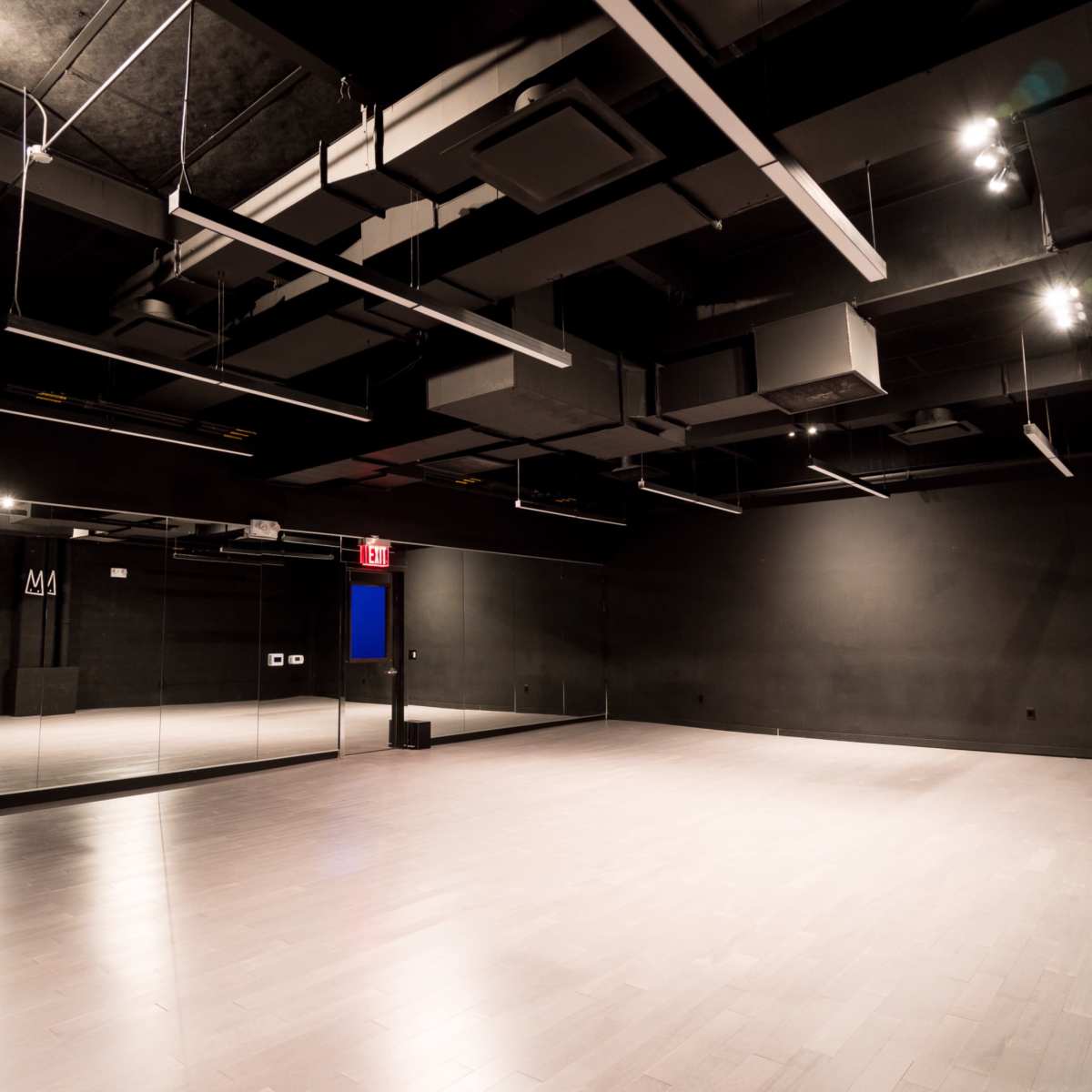 An empty dance studio with a large mirrored wall and recessed lighting against a dark backdrop.