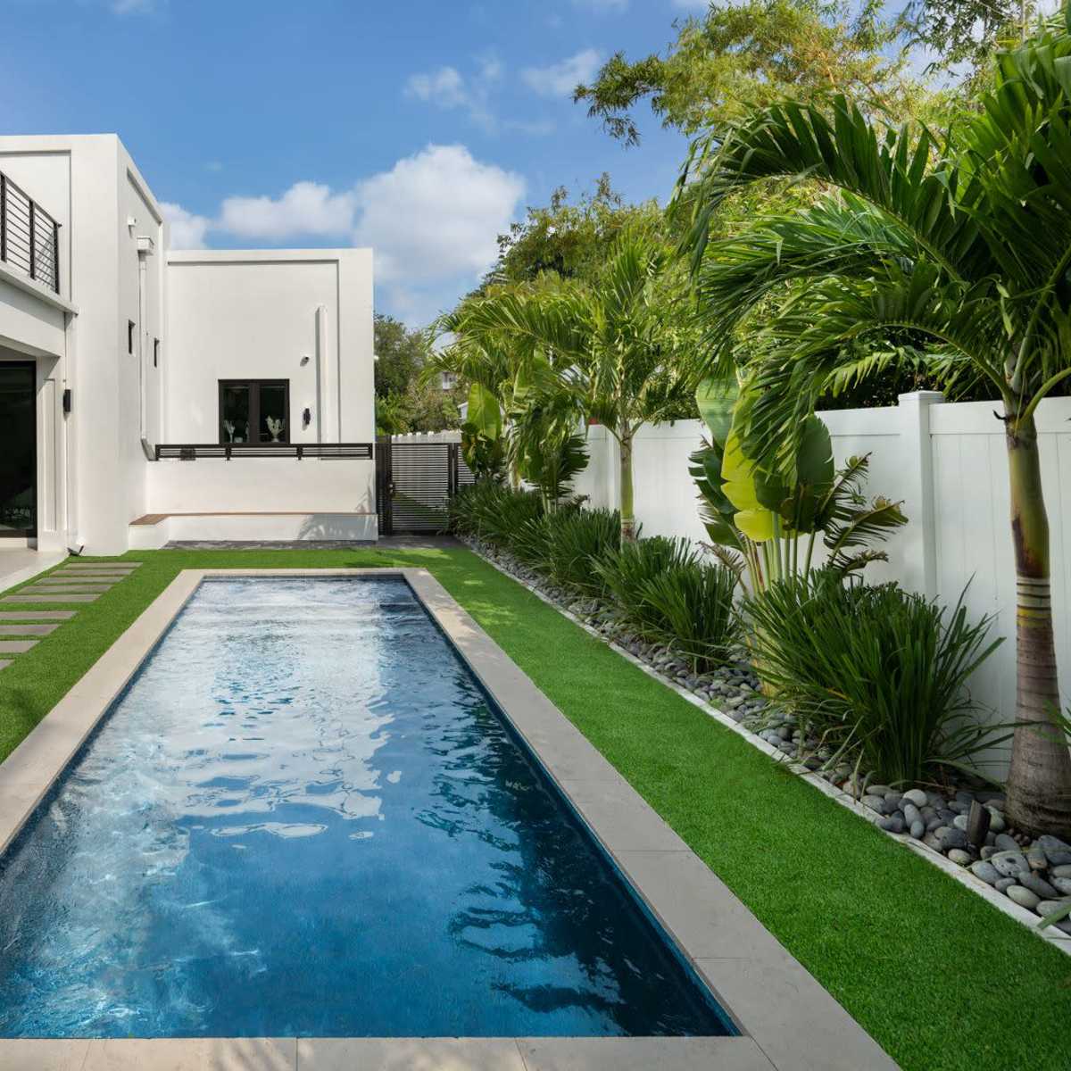 A modern house with a narrow swimming pool surrounded by landscaped greenery and artificial grass.