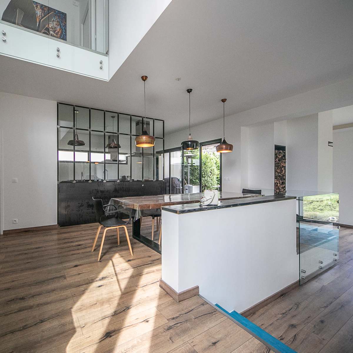 A modern open-concept interior with a dining area, a kitchen with a glass counter, and large windows allowing natural light.