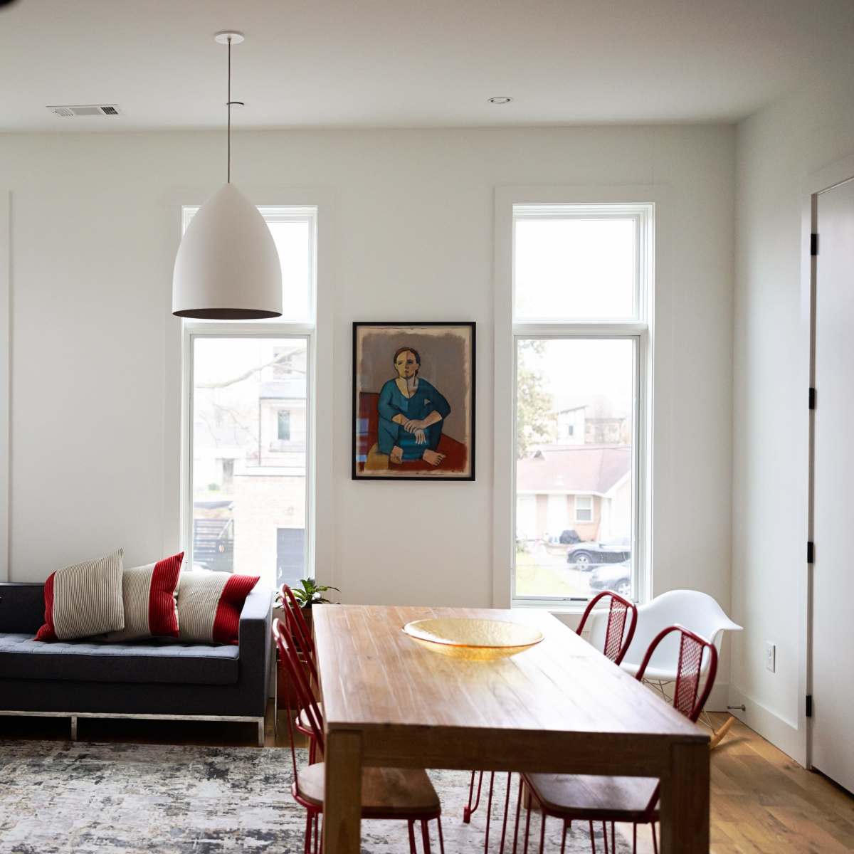 A modern living room with a sectional sofa, a wooden dining table surrounded by red chairs, and a framed artwork on the wall.