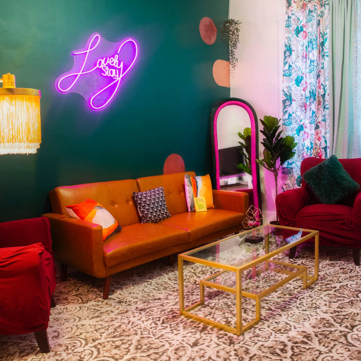 A cozy living room features a vibrant green wall, a neon sign, a brown leather sofa, and decorative curtains near a window.