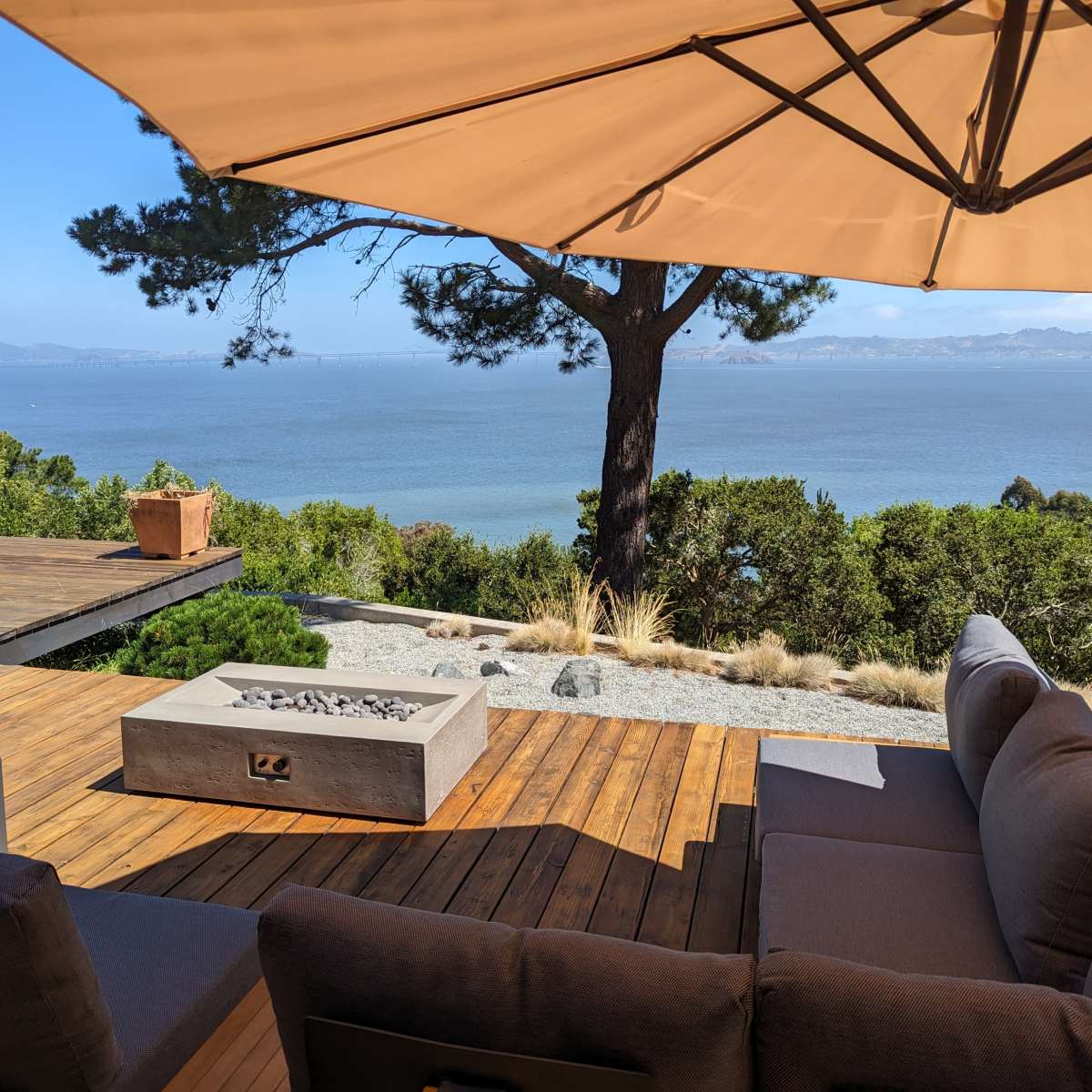 A shaded patio with a view of the water is set with a fire pit and comfortable seating.