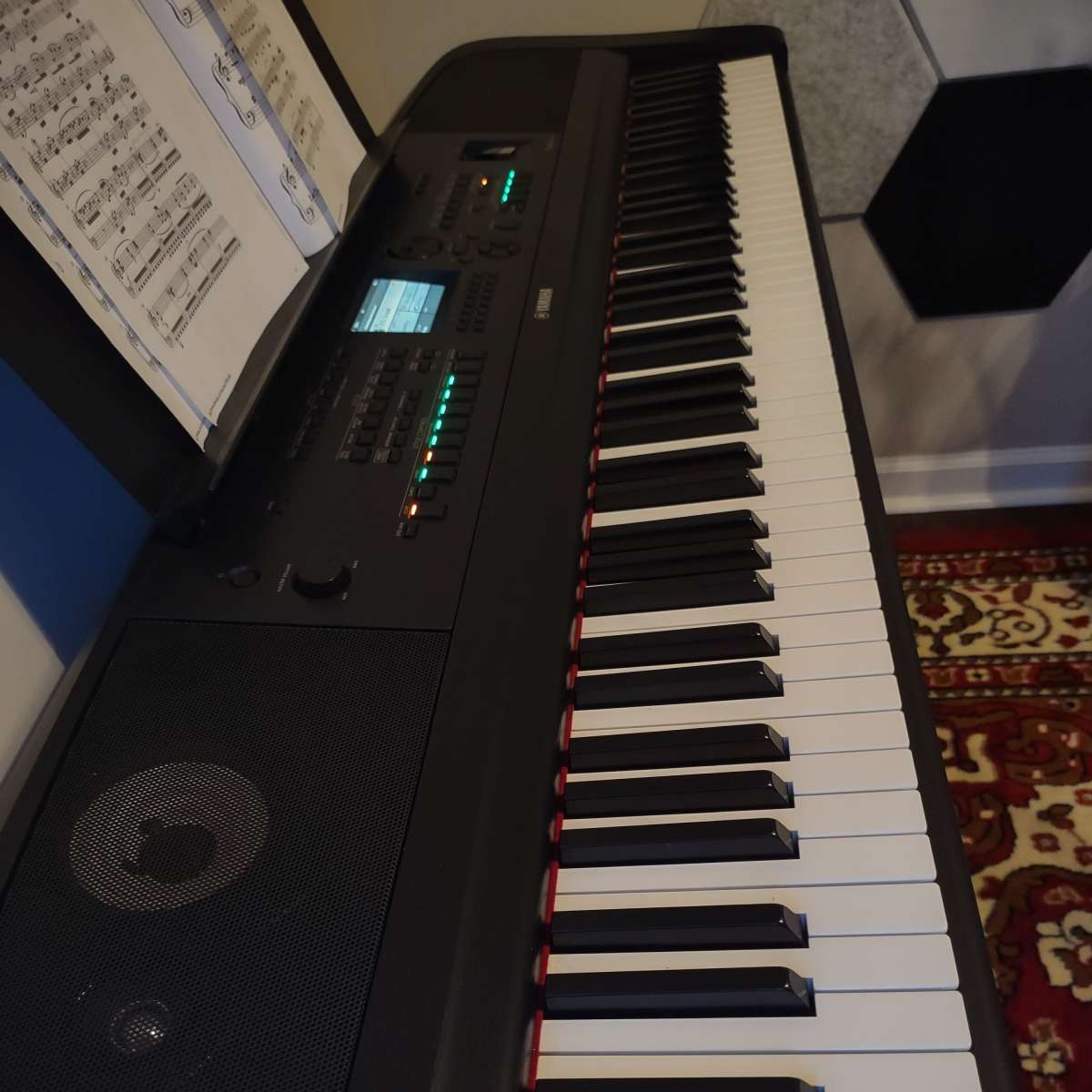 A black digital piano with visible keys, a control panel, and sheet music displayed above it.