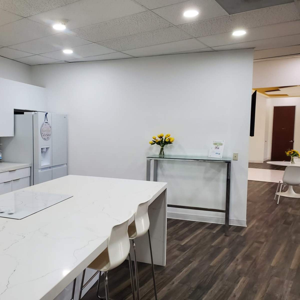 A modern kitchen with a large island, a refrigerator, and a glass table, featuring white cabinetry and a hexagonal tile backsplash.