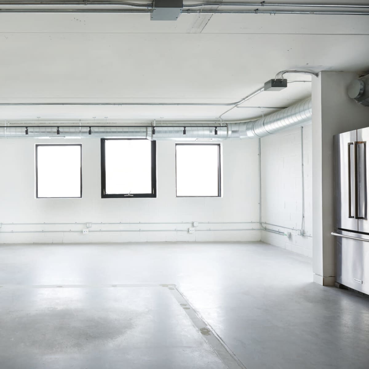 An empty room features a long, white counter and three large windows along one wall.