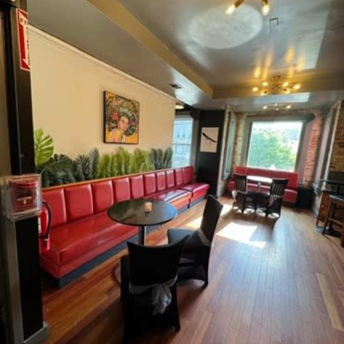 A cafe interior with red seating along the wall, a round table with black chairs, and large windows letting in natural light.