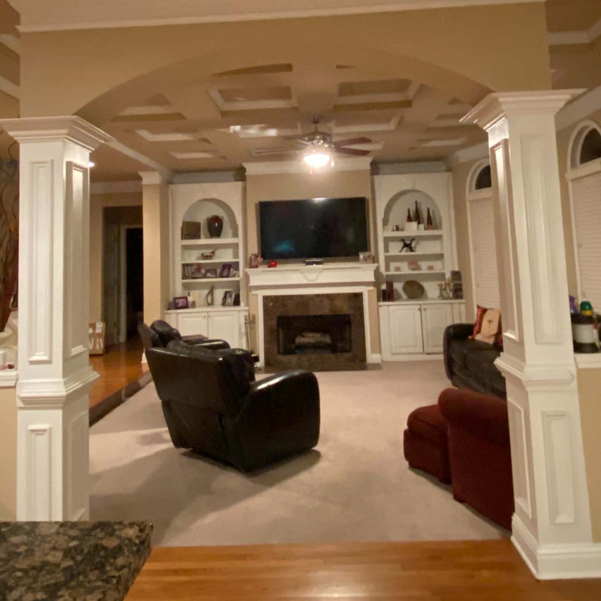 A living room with a TV mounted above a fireplace, framed by white columns and featuring a black recliner and a red sofa.