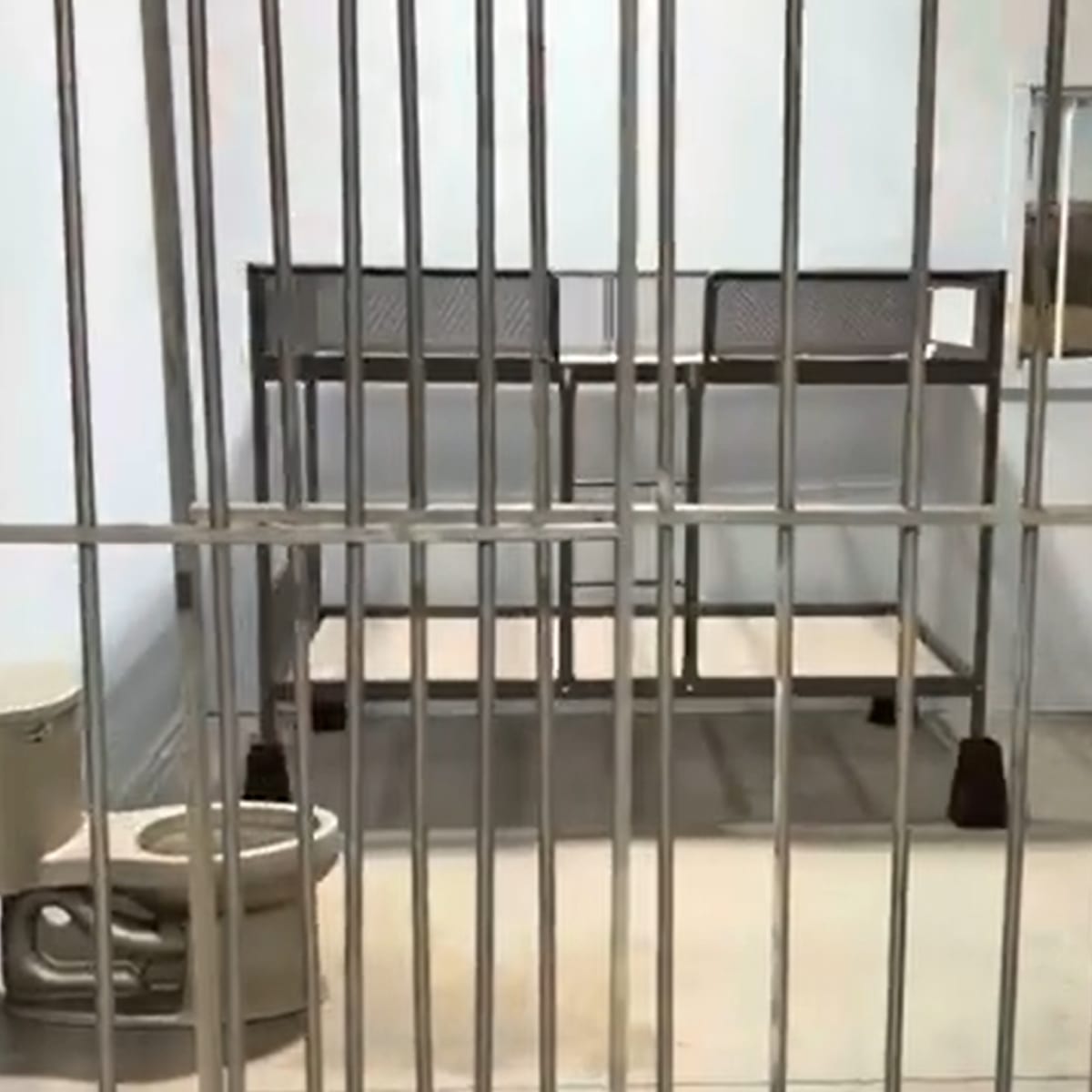 The interior of a jail cell, featuring a bunk bed, a toilet, and barred windows.