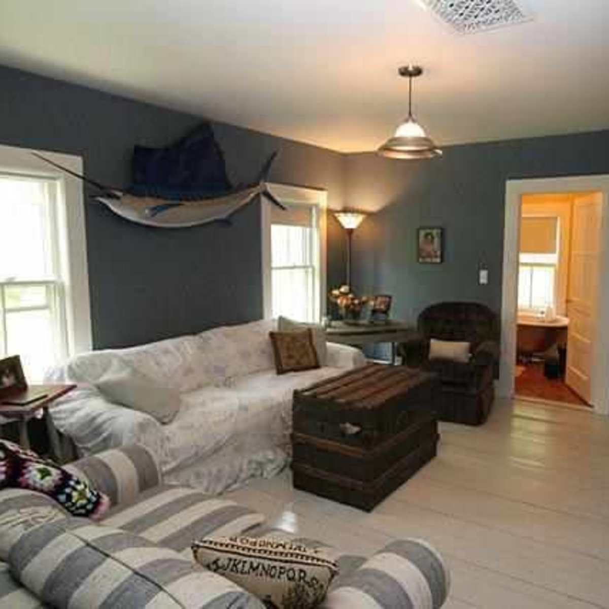 A living room with light-colored furniture, a wooden coffee table, and a hallway leading to a bathroom.