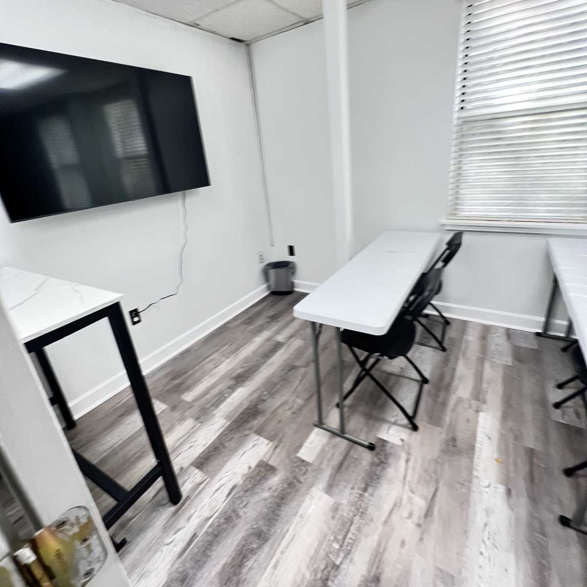 A small, sparsely furnished classroom with a large TV mounted on the wall and two tables with chairs.