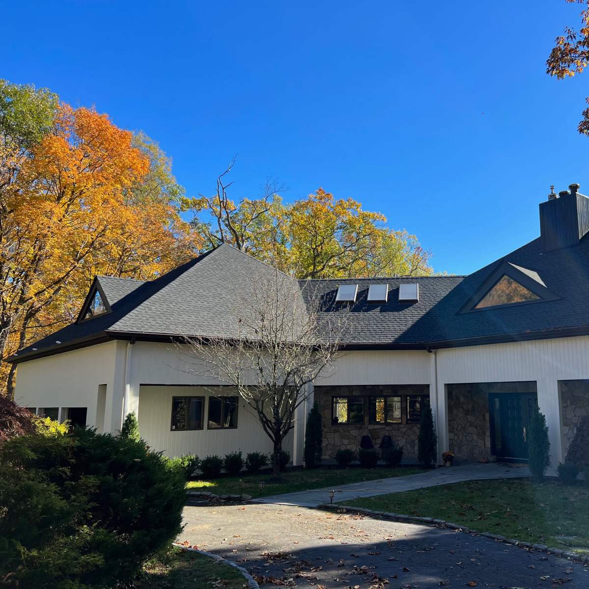 A modern house with a sloped roof and stone accents is surrounded by colorful autumn foliage.