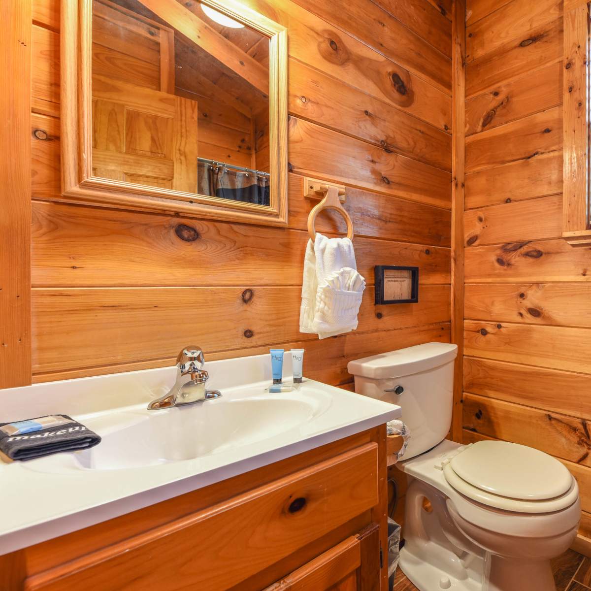 A bathroom with wooden walls, a sink with a mirror above, a toilet, and neatly arranged towels.