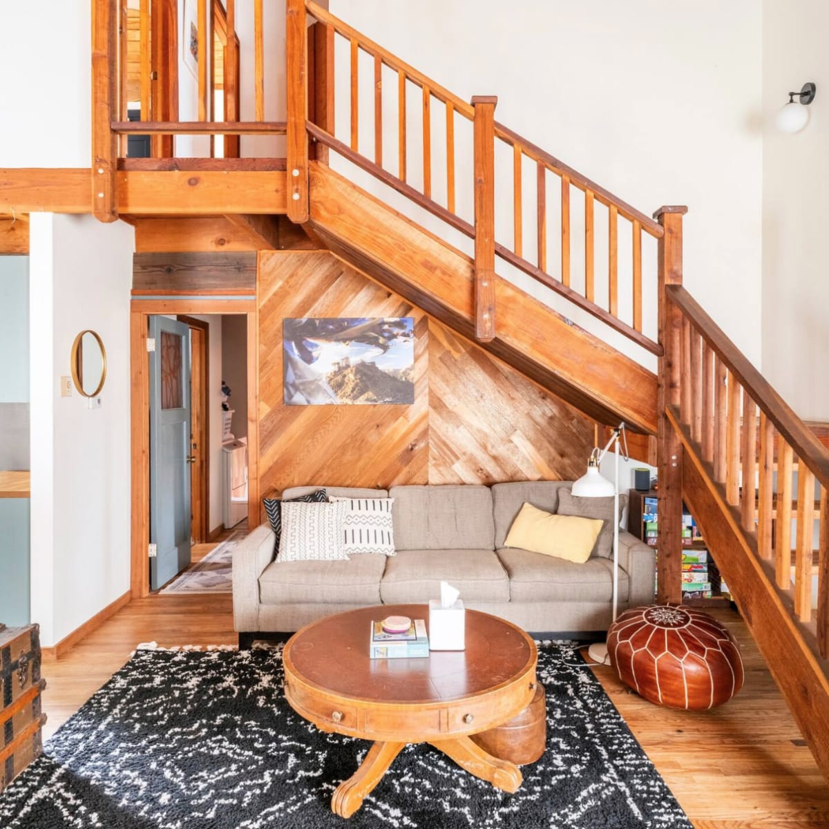 A spacious living room with a wooden staircase, a couch, a round coffee table, and a patterned rug.