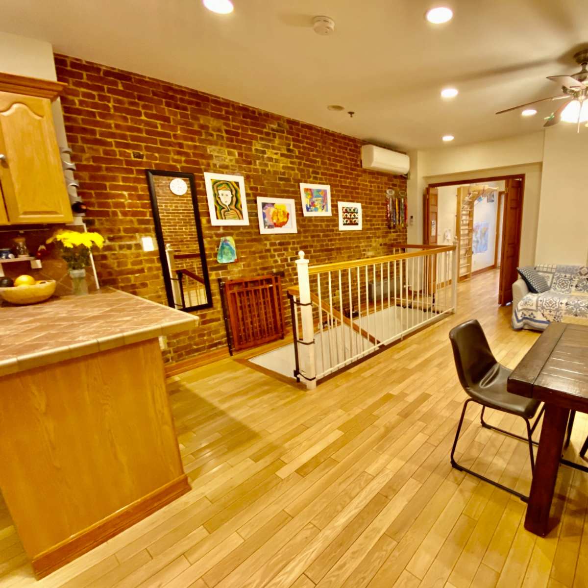 An open-concept living space featuring a kitchen area with wooden cabinets, a dining table, a seating area with a couch, and exposed brick walls.