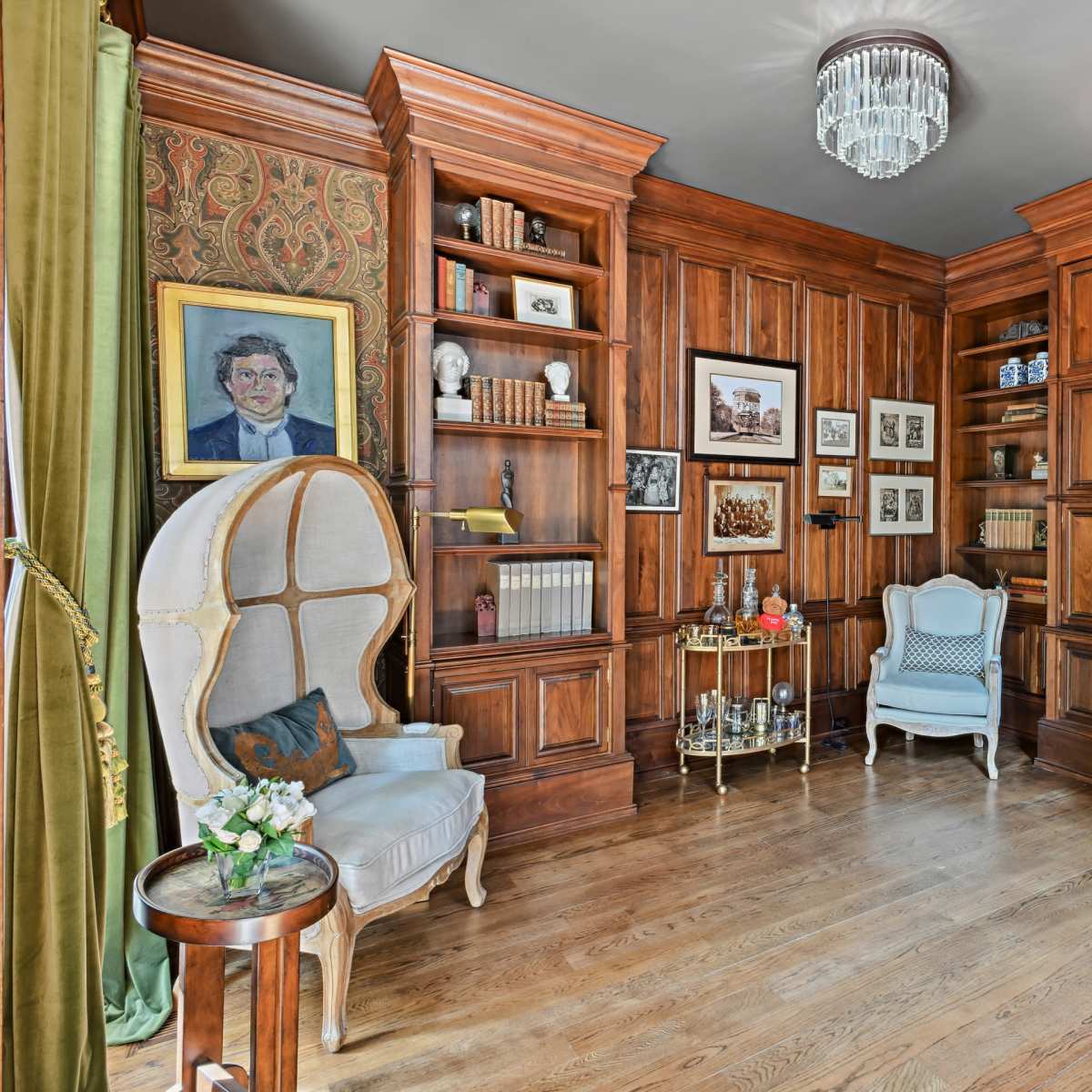A wooden library with built-in bookshelves, two light-colored chairs, and a decorative display table.