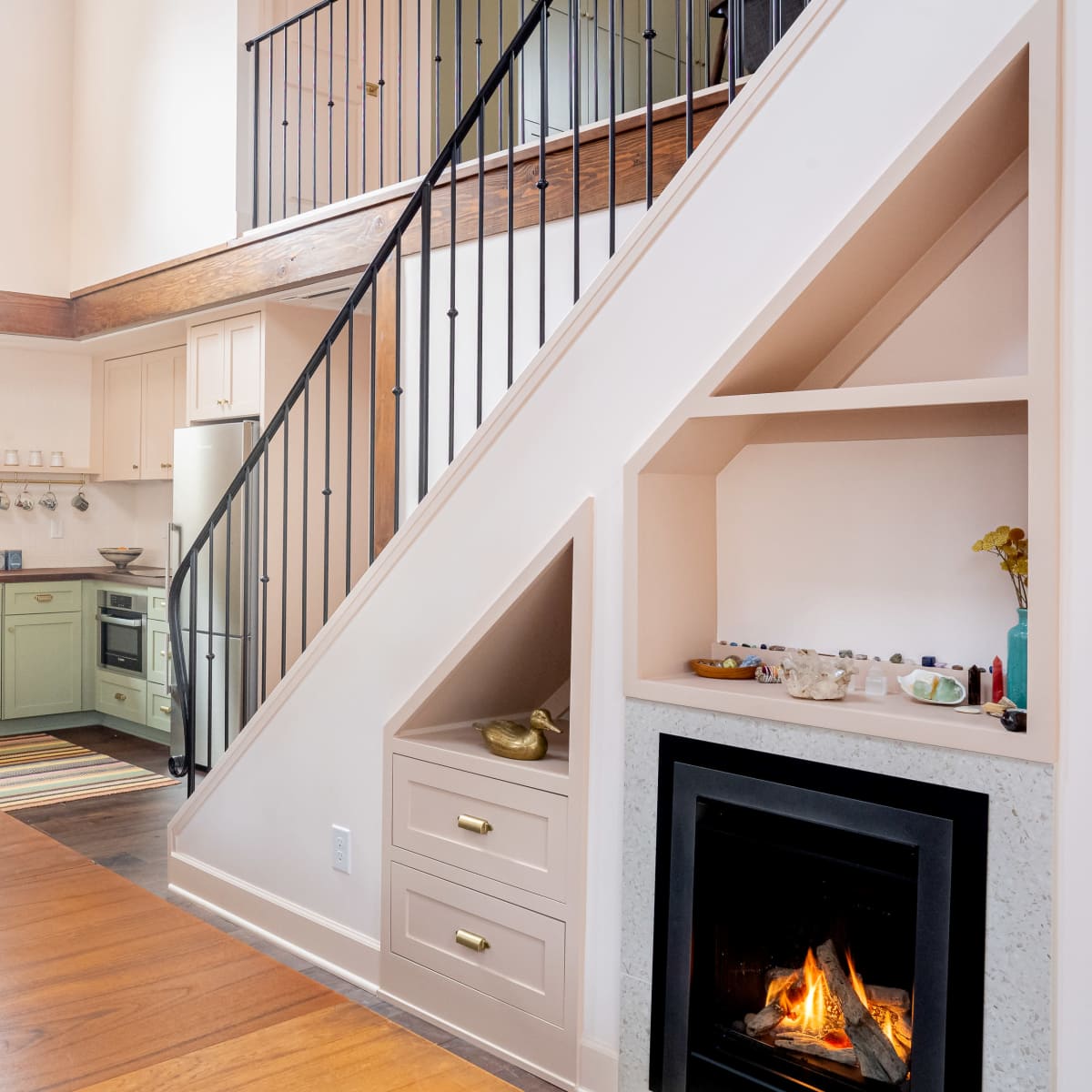 A modern kitchen with green cabinets and a staircase leading to an upper level, alongside a fireplace built into the wall.
