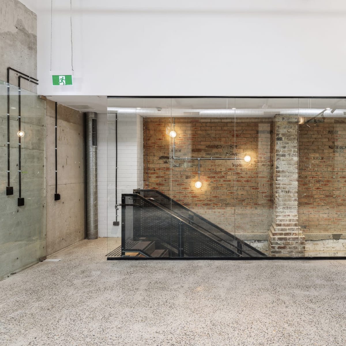 A modern interior space featuring a glass-walled staircase adjacent to exposed brick walls and industrial lighting.