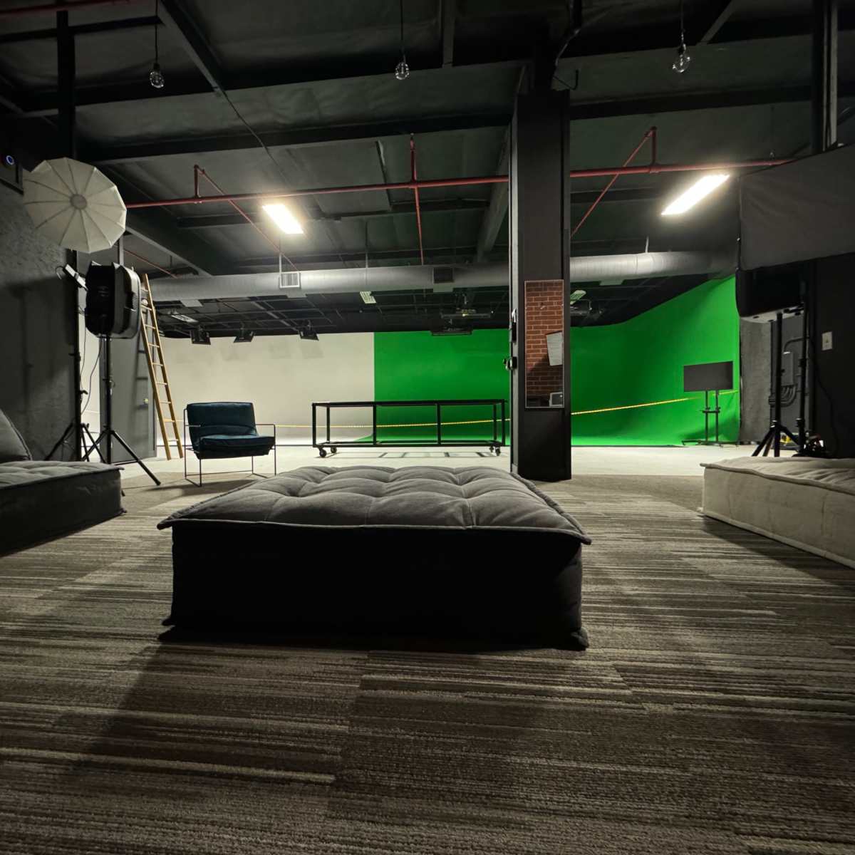 A spacious studio interior with seating arrangements and a green screen backdrop for video production.