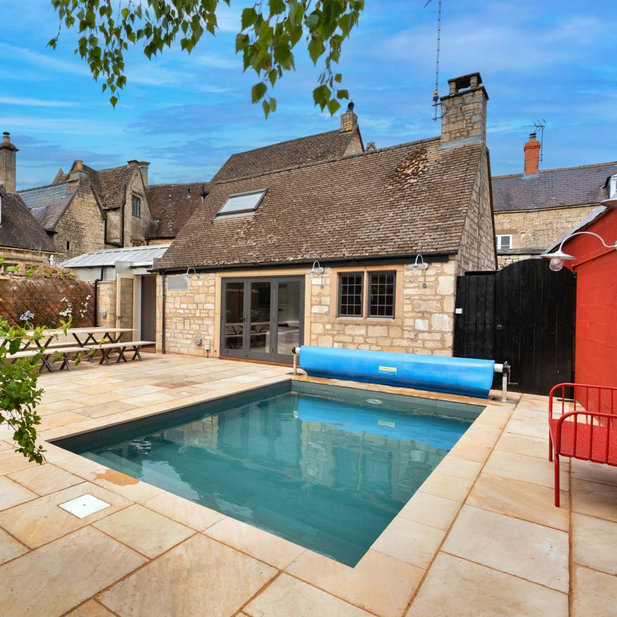 A small rectangular swimming pool surrounded by stone tiles and a seating area adjacent to historical-style buildings.
