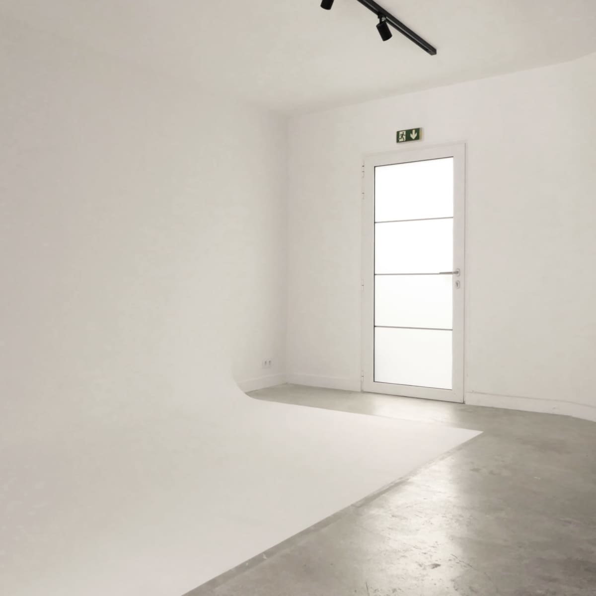 A minimalist room with a white backdrop, concrete flooring, and a glass door.