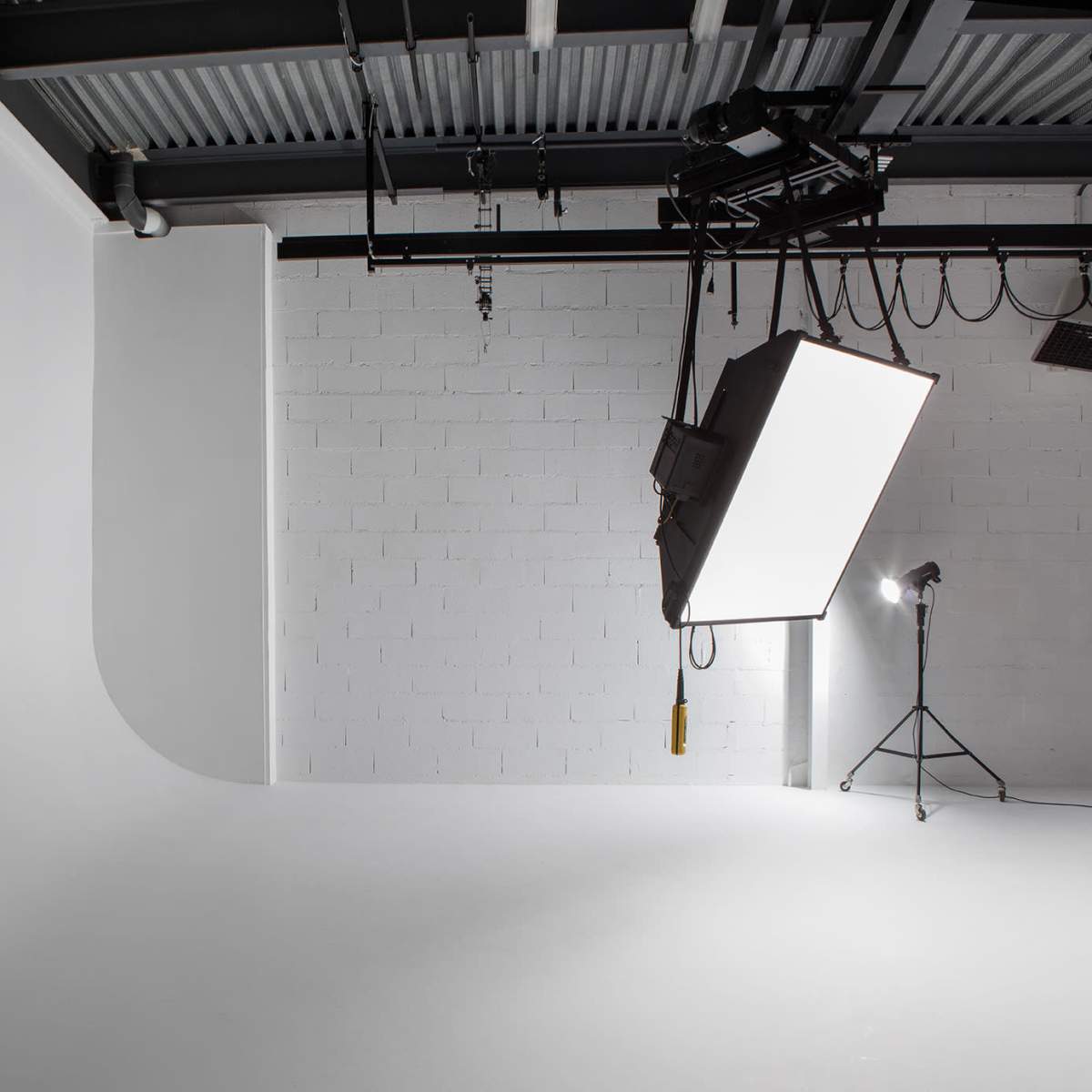 A minimalistic photography studio with a curved white backdrop and overhead lighting equipment.