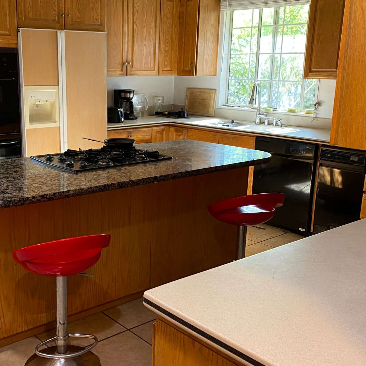 The kitchen features a central island with a granite countertop, two red bar stools, and various appliances including a microwave and coffee maker.