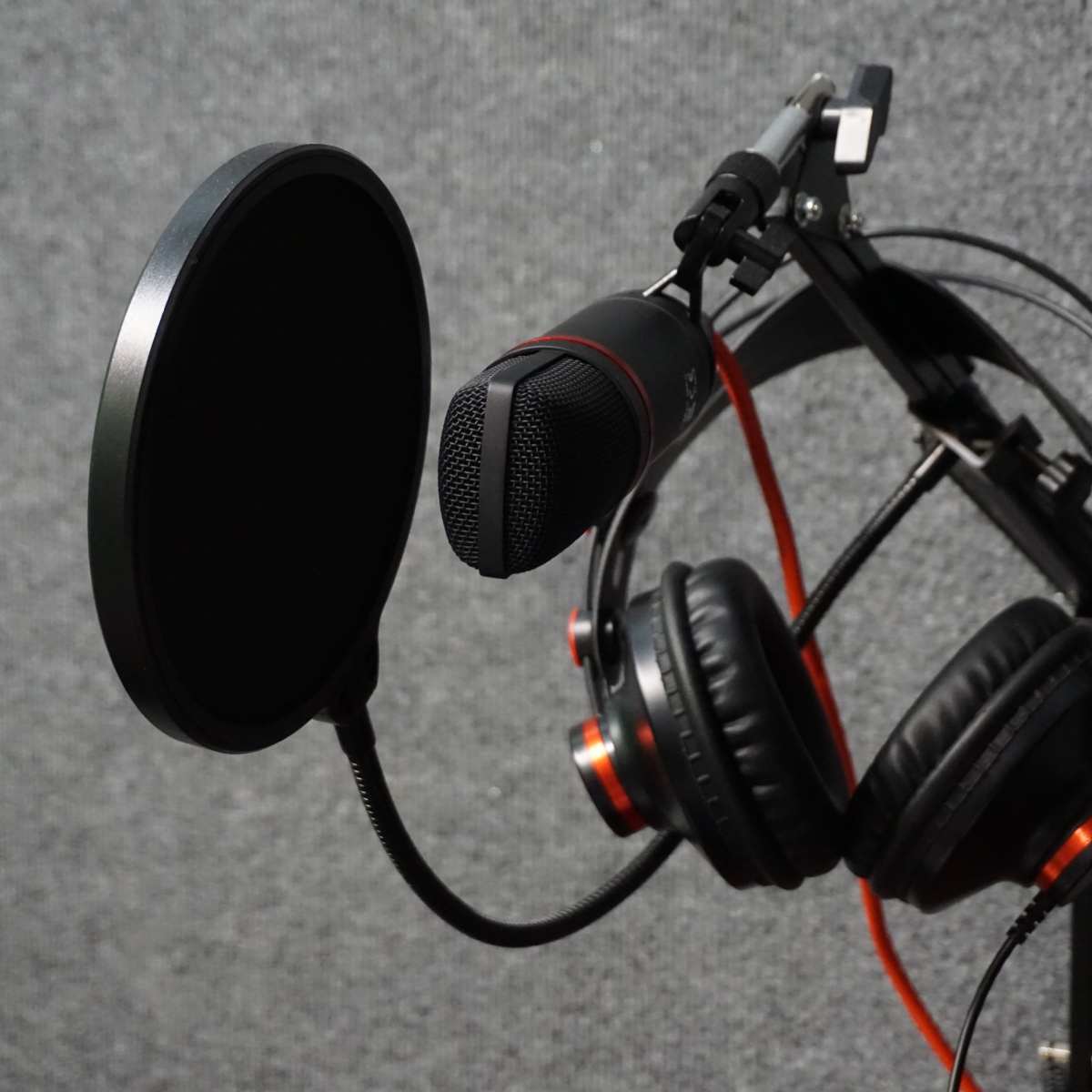 A microphone and a pair of headphones are mounted on a stand against a textured gray background.
