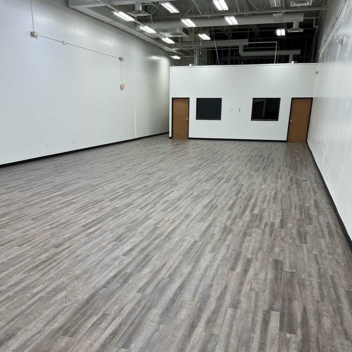 A large, empty room with wooden floors and two windows along the far wall.